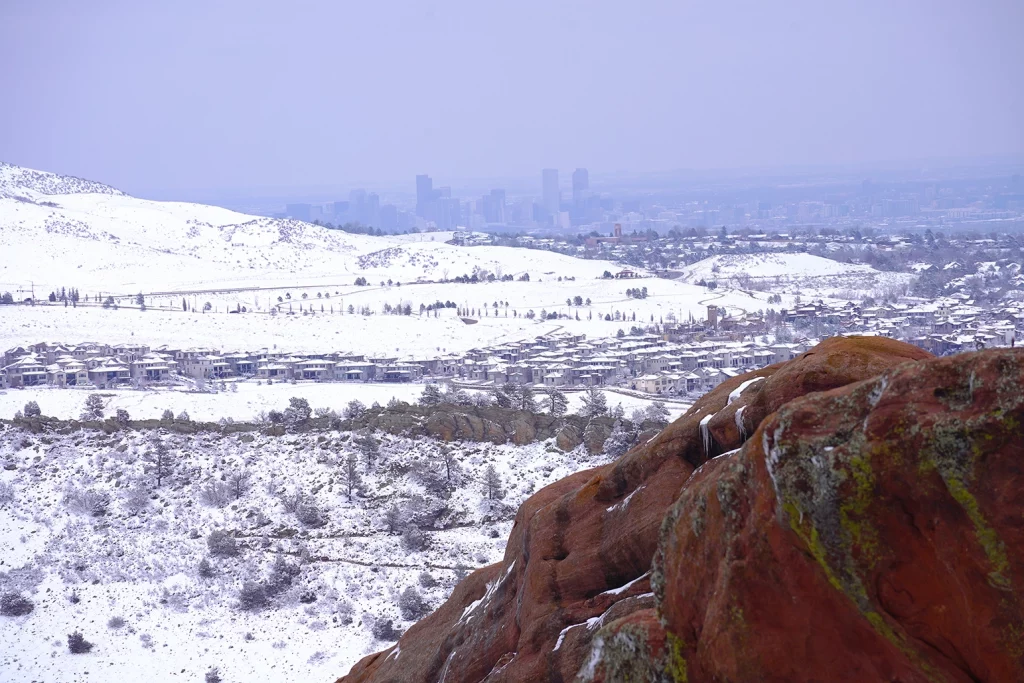 Verschneite Hügellandschaft bei Red Rocks mit der Skyline von Denver im Hintergrund.