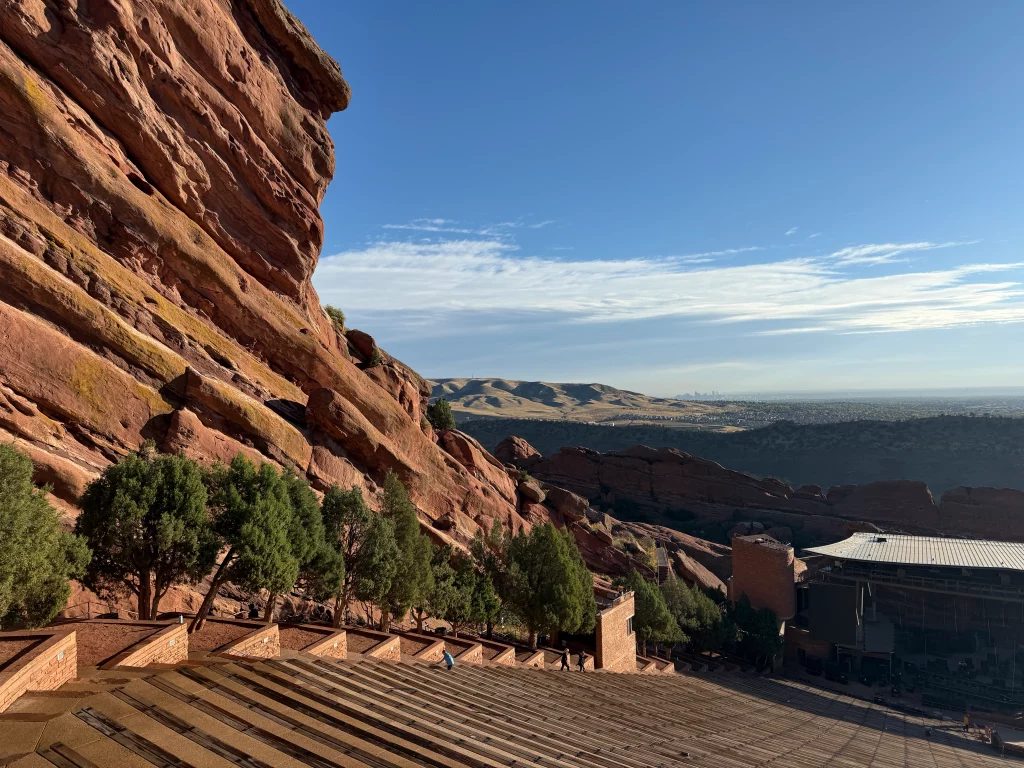 Blick über die roten Felsformationen des Red Rocks Amphitheatre mit der Skyline von Denver im Hintergrund.