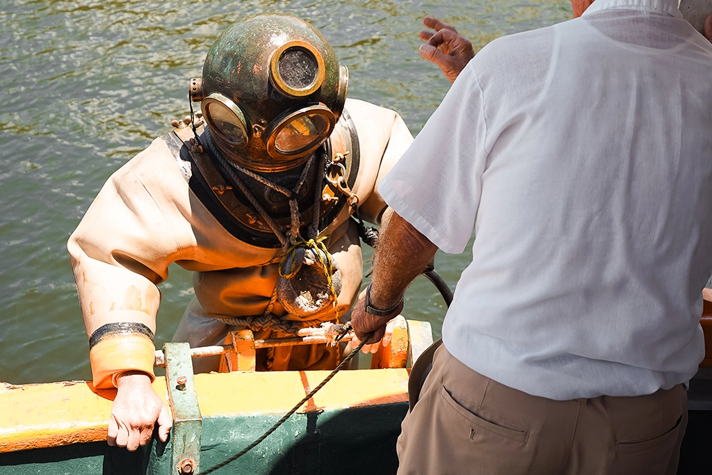 Schwammtaucher mit historischem Kupferhelm steigt von einem Boot der St. Nicholas Boat Line in den Anclote River.