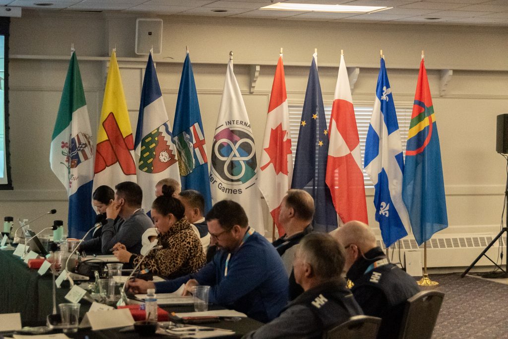 Sitzung des Arctic Winter Games International Committee mit Flaggen der teilnehmenden Regionen.