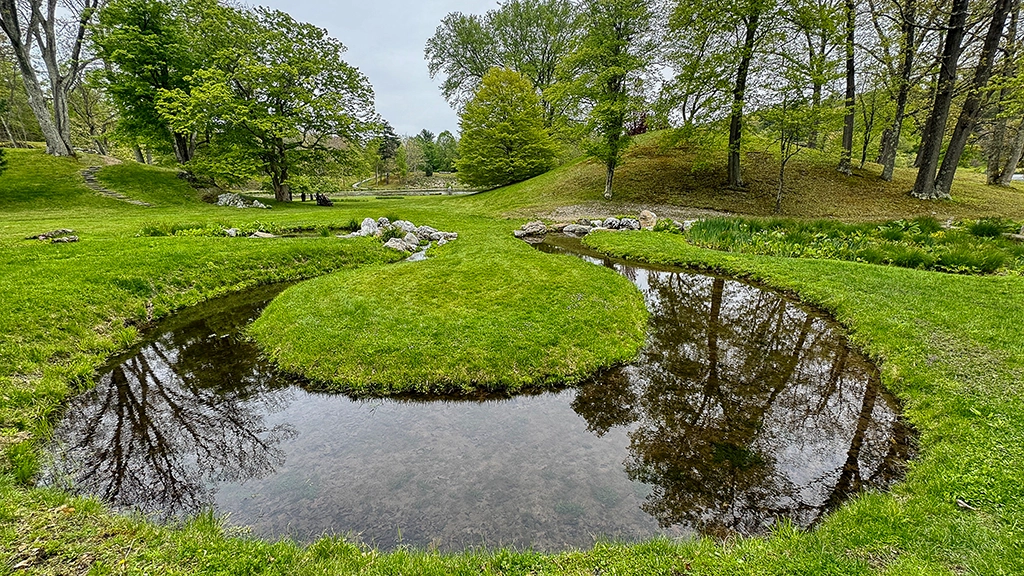 Geschwungener Wasserlauf mit kleiner Raseninsel im Innisfree Garden in Millbrook, New York.