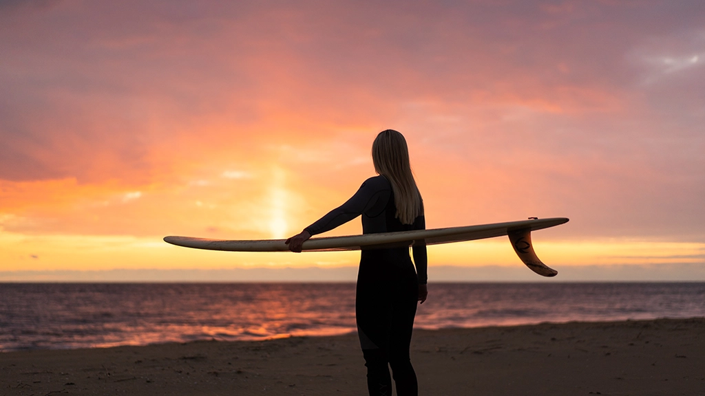 Surferin mit Surfbrett am Strand von Virginia Beach bei Sonnenuntergang.