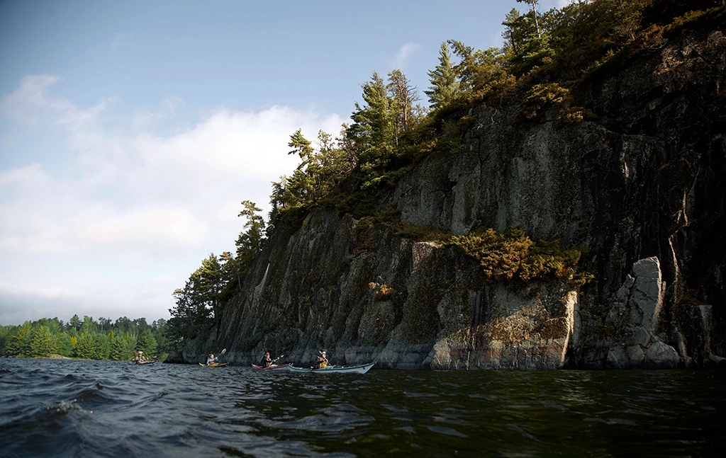 Paddler mit Kanus vor einer bewaldeten Felswand im Voyageurs National Park im Norden Minnesotas.