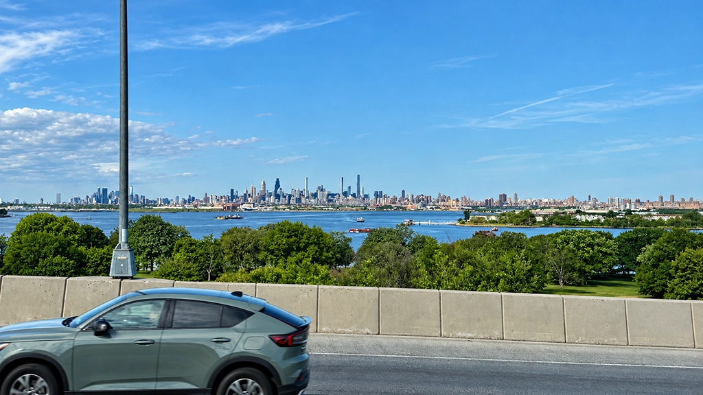 Blick über Wasser und Bäume auf die Skyline von Manhattan in New York City bei blauem Himmel