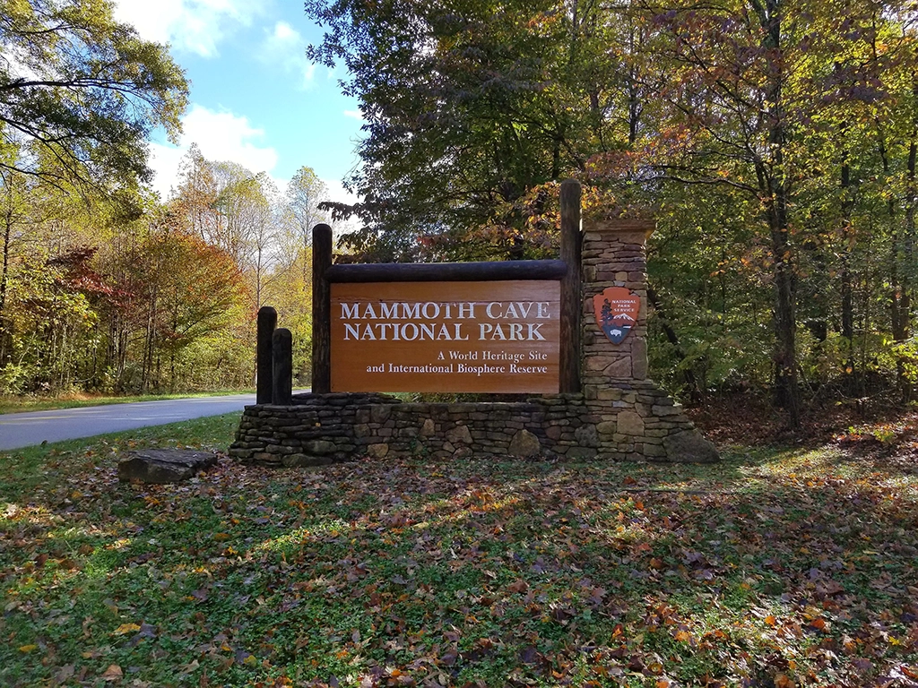 Eingangsschild des Mammoth Cave National Park in Kentucky in herbstlicher Waldlandschaft.