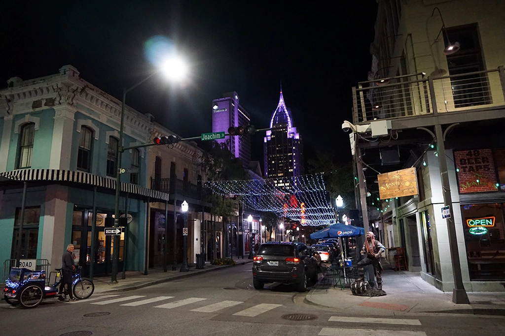 Nächtliche Dauphin Street in Downtown Mobile mit historischen Fassaden und beleuchteter Skyline.