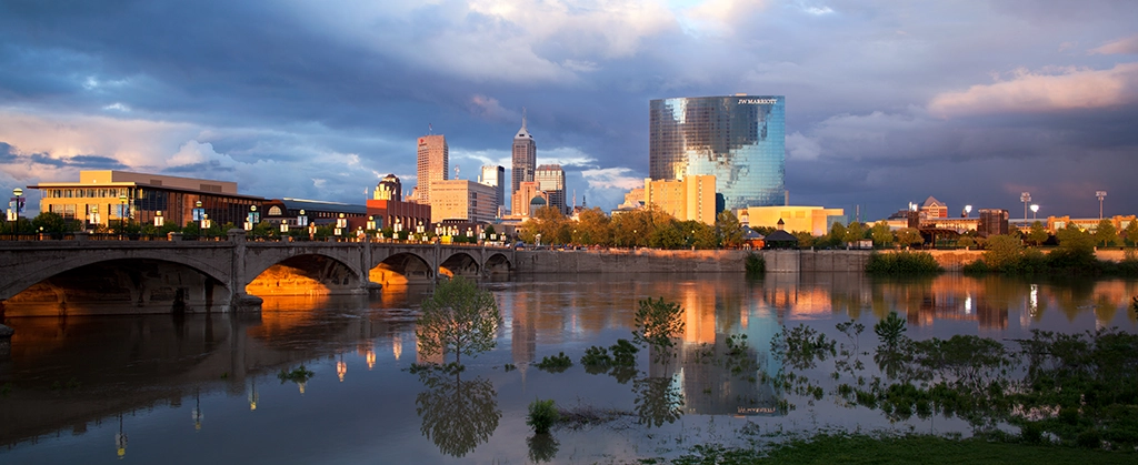 Skyline von Downtown Indianapolis am White River mit Brücke und Spiegelungen im Wasser.