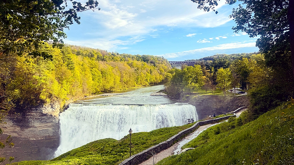 Middle Falls des Genesee River im Letchworth State Park mit bewaldeter Schlucht, Wanderweg und Eisenbahnbrücke im Hintergrund.