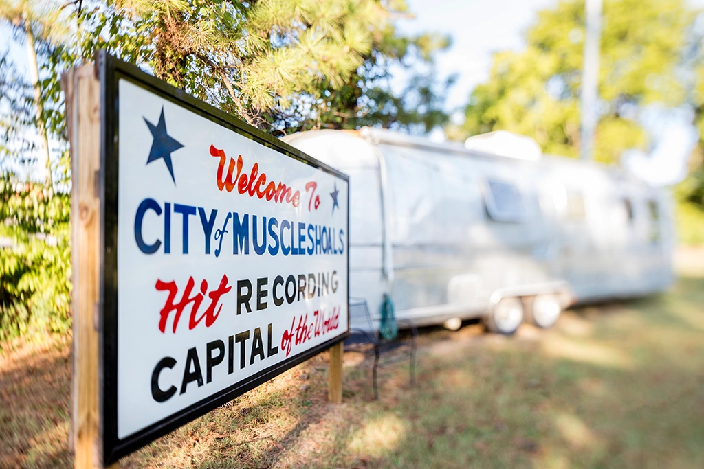 „Welcome to City of Muscle Shoals“-Schild mit dem Schriftzug „Hit Recording Capital of the World“ vor einem historischen Wohnwagen in Alabama.