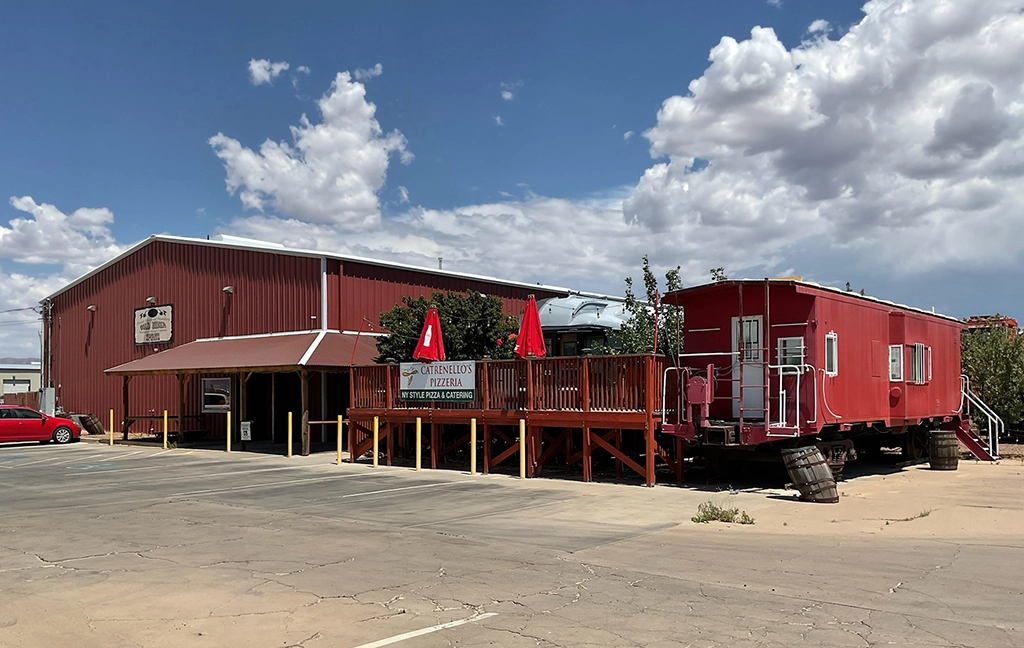 Außenansicht der Desert Diamond Distillery in Kingman, Arizona, mit rotem Eisenbahn-Caboose, Holzterrasse und angeschlossener Pizzeria an der Route 66.