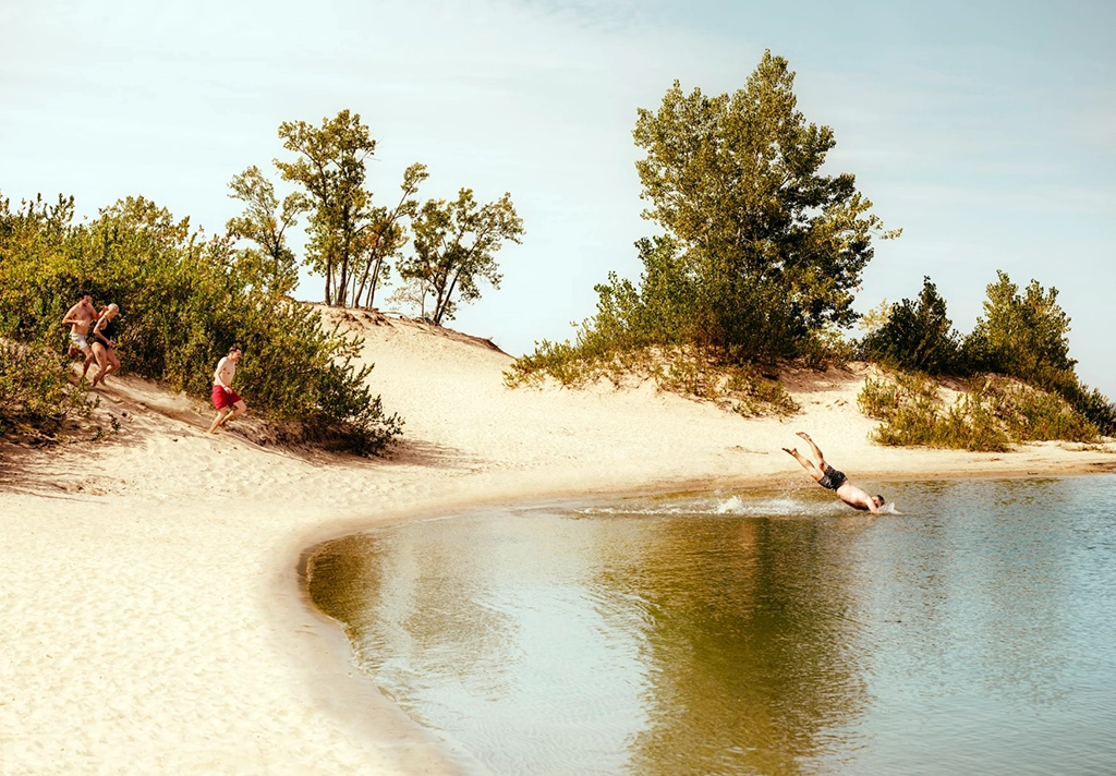 Badegäste springen von einer Sanddüne ins Wasser im Sandbanks Provincial Park in Prince Edward County, Ontario