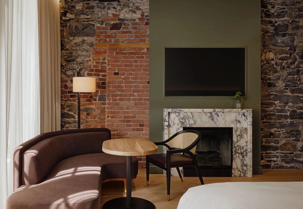 Modernes Gästezimmer im Hôtel Nelligan in Montréal mit freigelegten Backstein- und Natursteinwänden, Kamin und eleganter Sitzecke
