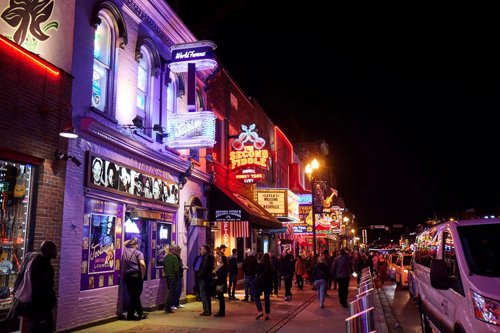 Neonbeleuchtete Honky-Tonk-Bars und zahlreiche Besucher am Abend auf dem Broadway in Nashville, Tennessee.