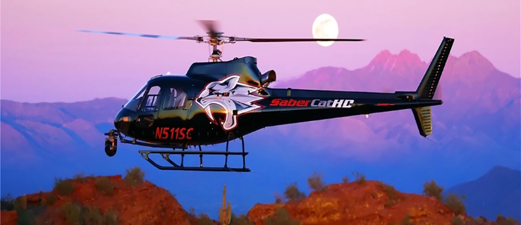 Helikopter von H5 Helicopters vor einer Bergkulisse bei Sonnenuntergang in der Sonora-Wüste bei Scottsdale, Arizona, mit dem Mond am Himmel.