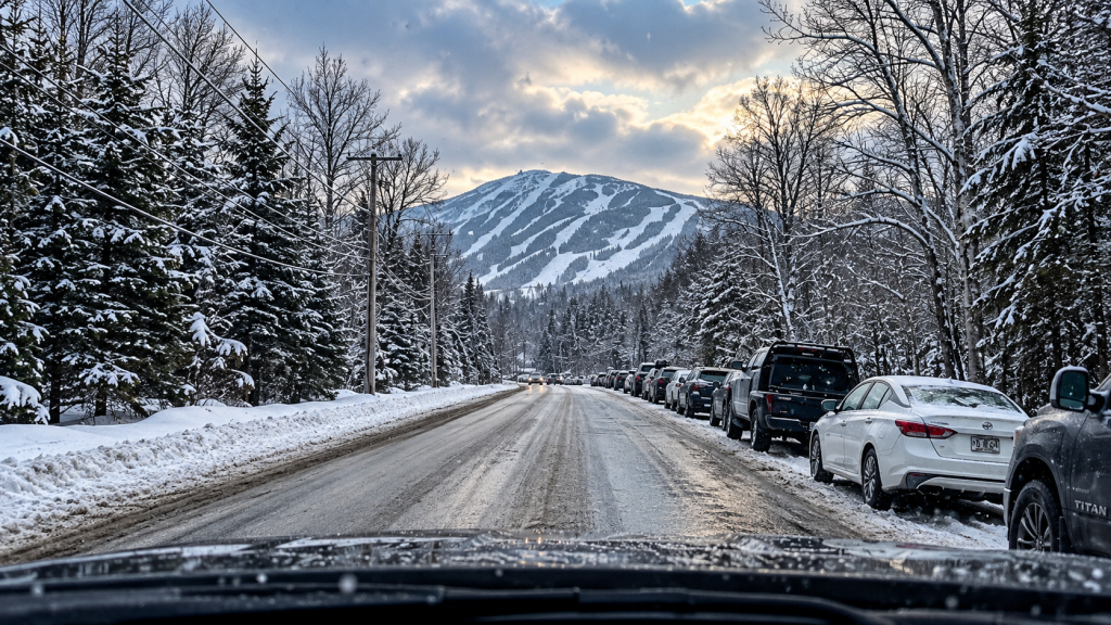 Winterliche Anfahrt zum Skigebiet Sugarloaf in Maine: Verschneite Straße durch das Carrabassett Valley mit Blick auf den Berg und seine Skipisten.