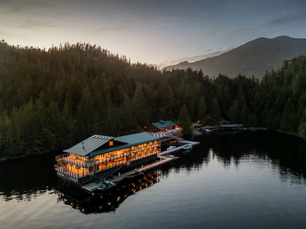 Schwimmende Wahous Wilderness Lodge in der Quait Bay auf Vancouver Island bei Abenddämmerung, umgeben von dichtem Küstenregenwald und Bergen