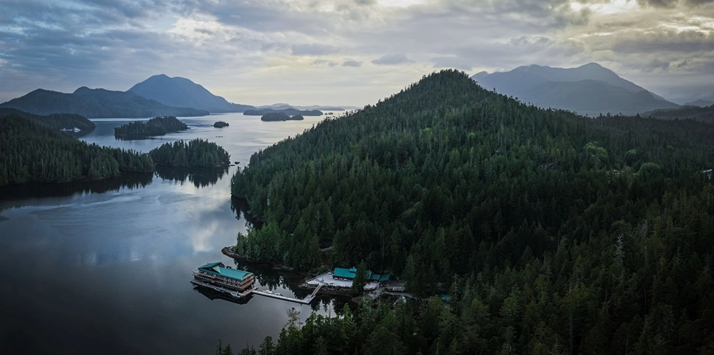 Luftaufnahme der Wahous Wilderness Lodge in einer bewaldeten Bucht des Clayoquot Sound mit Inseln, Bergen und Pazifikküste auf Vancouver Island