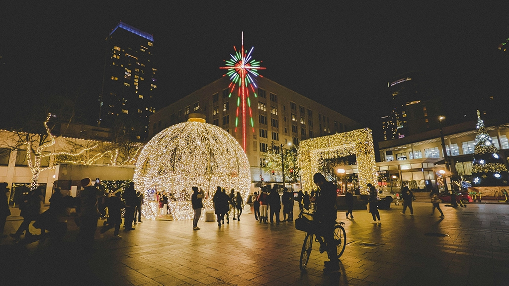 Festlich beleuchteter Platz in Downtown Seattle mit großer Lichterkugel, Weihnachtsbaum und zahlreichen Besuchern am Abend.